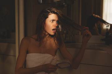 Close up of sad young woman in white towel brush her damaged and tangled wet hair. Morning routine....