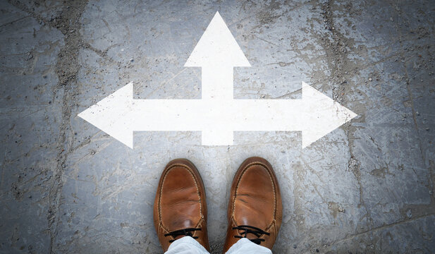 Brown leather shoes and chalky arrows in three directions on asphalt - choice concept