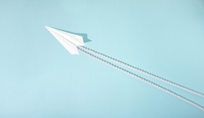 Paper white airplane with pearl trail isolated on blue background. Flat lay travel creative concept.