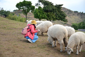 A female tourist in a bright orange duck down jacket wearing a yellow hat sits down and takes a...