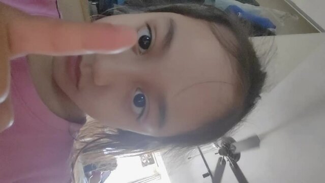The little girl is practicing to do crossed eyes at home. Vertical video.