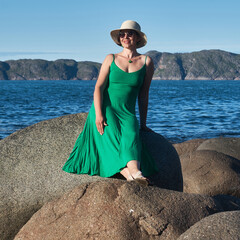 Woman tourist in a straw hat and a green dress on the seashore on a bright sunny day