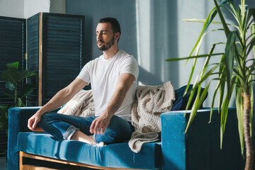 Relaxed young man resting comfortable on couch breathing fresh air. Peace of mind concept. Cozy apartment. - obrazy, fototapety, plakaty
