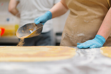 Fototapeta premium The kitchen in the bakery - the process of making cinnabons, the woman baker adds cinnamon and chocolate to the dough