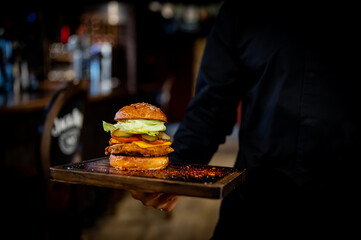 Men's waiter hands hold a tray with a chicken burger in pub