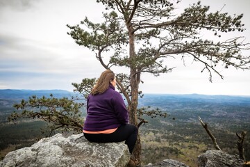 Naklejka na ściany i meble woman sitting on cliff edge after hiking up Cheaha State Park Mountain, highest point in Alabama