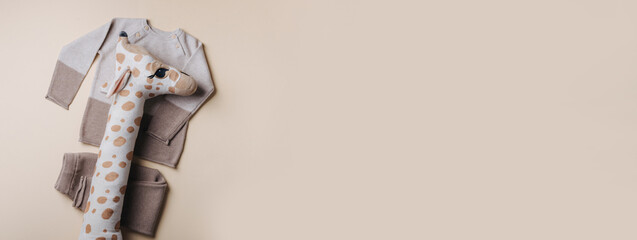 Knitted brown, beige sweater and giraffe soft toy. Set of baby stuff and accessories for newborn on pastel background. Baby shower or baby care concept. Fashion newborn. Flat lay, top view. Banner