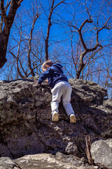 Young toddler boy crawling along rock boulders while hiking up Cheaha mountain in Alabama state park and campground