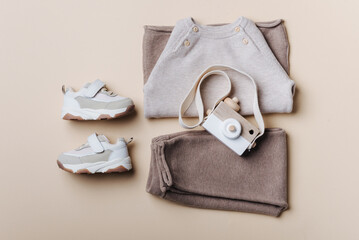 Baby stuff and accessories. Set of knitted clothes - sweater, pants, shoes, wooden camera toy. Baby shower concept. Flat lay, top view. Copy space. Fashion children's clothing, shoes