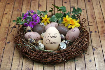 Dekoratives Osternest mit Blumen und einem beschrifteten Osterei mit dem Text Frohe Ostern.