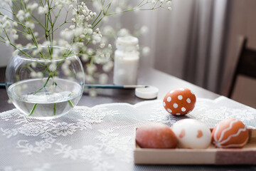 Pastel-coloured Easter eggs lie on the table on a pretty napkin beside small white flowers and a brush of white paint