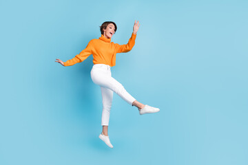 Fototapeta na wymiar Full body photo of attractive young woman jump dance enjoy lightness elegant dressed stylish orange look isolated on blue color background