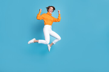Fototapeta na wymiar Full body photo of attractive young woman raise fists shout yeah jump crazy dressed stylish orange look isolated on blue color background