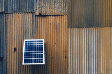 Solar panel attached on old zinc wall. Electric solar panel on the house wall. Small solar panel mounted on an outdoor galvanized wall with copy space. Using renewable solar energy technology concept.