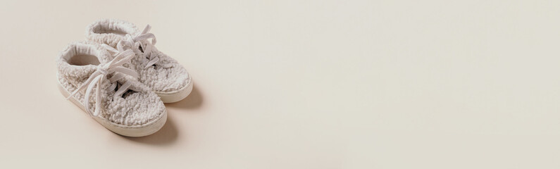 Gender neutral baby teddy shoes and accessories over beige background. Top view, copy space