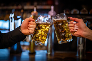 man and woman hands clinking with glasses of light beer at the pub or bar