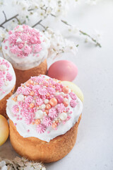 Traditional Easter sweet bread or cakes with white icing and sugar decor, colored eggs and cherry blossom tree branch over white table. Various Spring Easter cakes. Happy Easter day. Selective focus.