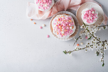 Fototapeta na wymiar Traditional Easter sweet bread or cakes with white icing and sugar decor, colored eggs and cherry blossom tree branch over white table. Various Spring Easter cakes. Happy Easter day. Selective focus.
