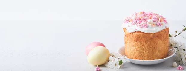 Traditional Easter sweet bread or cakes with white icing and sugar decor, colored eggs and cherry blossom tree branch over white table. Various Spring Easter cakes. Happy Easter day. Selective focus.