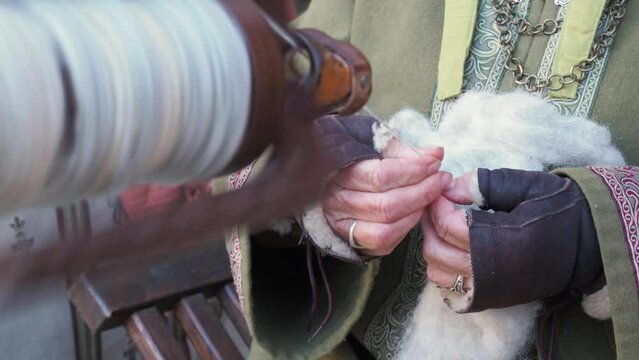 Closeup of female hands using an antique spindle spinning machine to weave raw wool