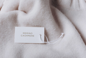Label with text Merino Cashmere on wool clothes. Tag composition of clothing on knitted texture...