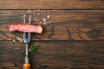Steaks T-bone. Slices of beef grilled meat barbecue steak on meat fork on burned dark wooden background with copy space for your text. Top view. Mock up.