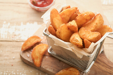 French fries in metal wire basket with salt and ketchup on old wooden light background clous up. Fried potatoes. Fast food and unhealthy food concept.