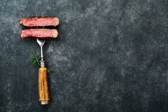 Steaks T-bone. Slices of beef grilled meat barbecue steak on meat fork on burned dark wooden background with copy space for your text. Top view. Mock up.