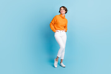 Fototapeta na wymiar Full length photo of lovely young lady look empty space shopping hands pockets wear trendy orange clothes isolated on blue color background