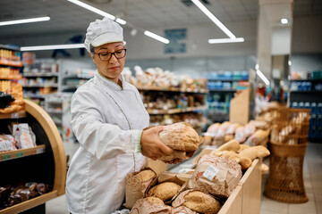 Supermarket baker arranging fresh bread on shelf.