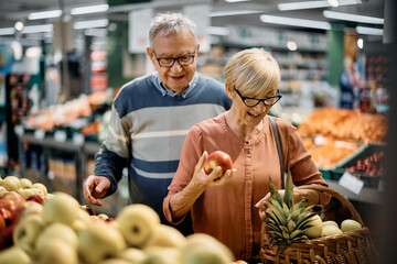 Happy senior couple buying fresh apples in supermarket.