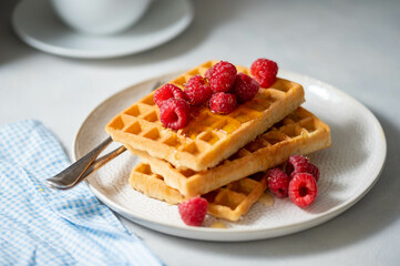 Closeup waffles with berries in plate served with cup of tea.