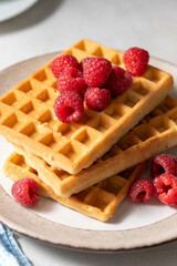 Breakfast waffles with berries in plate served with cup of tea.
