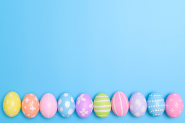 Happy Easter holiday greeting card design concept. Colorful Easter Eggs and spring flowers on blue background. Flat lay, top view, copy space.