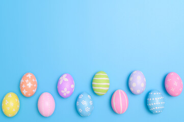 Happy Easter holiday greeting card design concept. Colorful Easter Eggs and spring flowers on blue background. Flat lay, top view, copy space.