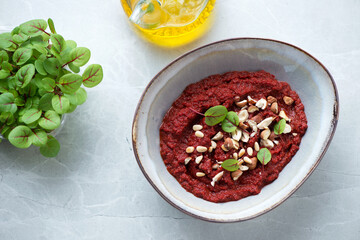 Bowl of beetroot caviar served with nuts and baby beetroot leaves, high angle view on a grey granite background, horizontal shot