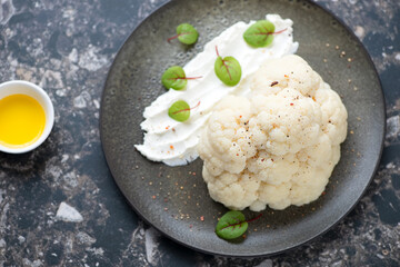 Half of steamed cauliflower head and cream-cheese, horizontal shot on a dark-brown granite background, elevated view