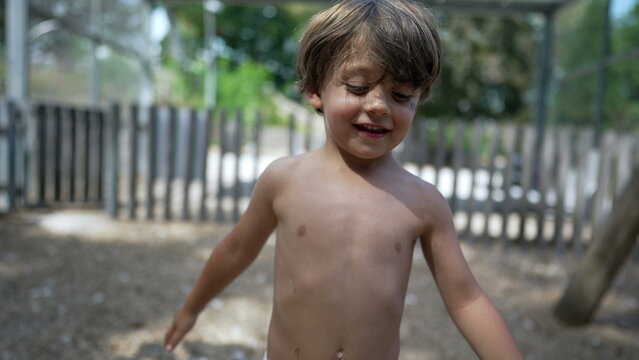Cute shirtless little boy playing outside smiling at camera standing at playground park throwing dirt in the air
