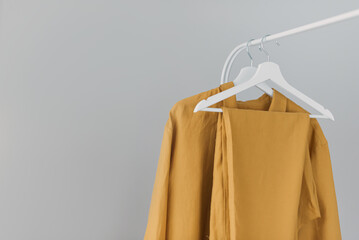 Clothing rack with stylish autumn outfit. Yellow, mustard color linen jacket, shirt and pajamas trousers dress on hangers in wardrobe. Woman wardrobe. Copy space