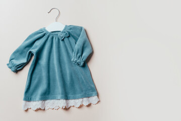 Blue dress for baby girl with white hanger on beige background. Set of baby clothes and accessories...