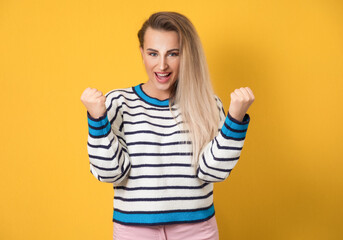 Excited woman yelling with opened mouth and clenched fists, isolated on yellow background....