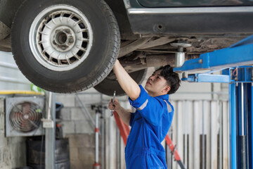 Portrait Shot of a Handsome Mechanic Working on a Vehicle in a Car Service. Professional Repairman is Wearing Gloves and Using a Ratchet Underneath the Car. Modern Clean Workshop.