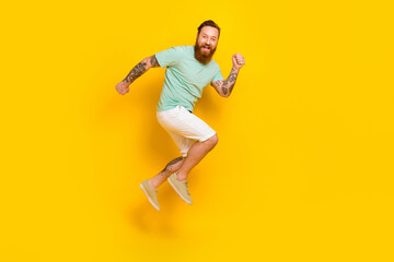 Fototapeta na wymiar Full length photo of funky running fast speed youngster guy red hairstyle beard wear green t-shirt shopping ad isolated on yellow color background