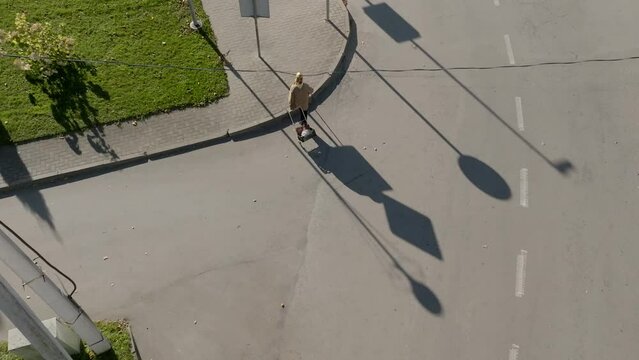 Aerial top view of a persom walking on the street and dragging a goods stroller