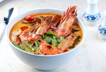 Tom Yam Kung or Tom Yum soup is Thai hot spicy soup shrimp or prawn with lemon grass, lemon, galangal, mushrooms, coconut milk and chili in bowl on wooden table top view, famous Thai food cuisine.