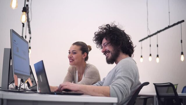 Young couple developers looking at laptop screen in office, discussing issues smiling