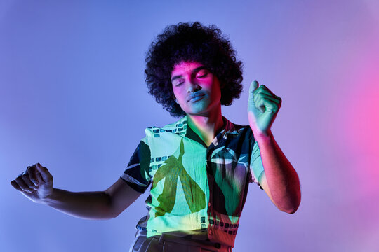 Ethnic guy dancing in studio illuminated by neon lights