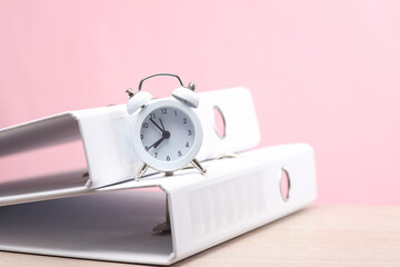 Office work, business concept. Alarm clock with folders on a pink background