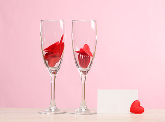 Two glass glasses with hearts and a white business card on a pink background. Valentine's Day, love concept