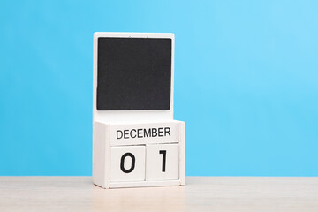 White wooden block monthly calendar with the date december 1 on the table, blue background....